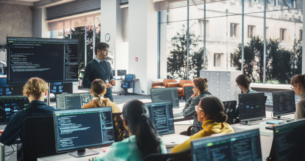 Teacher Giving Lesson to students sitting at computers
