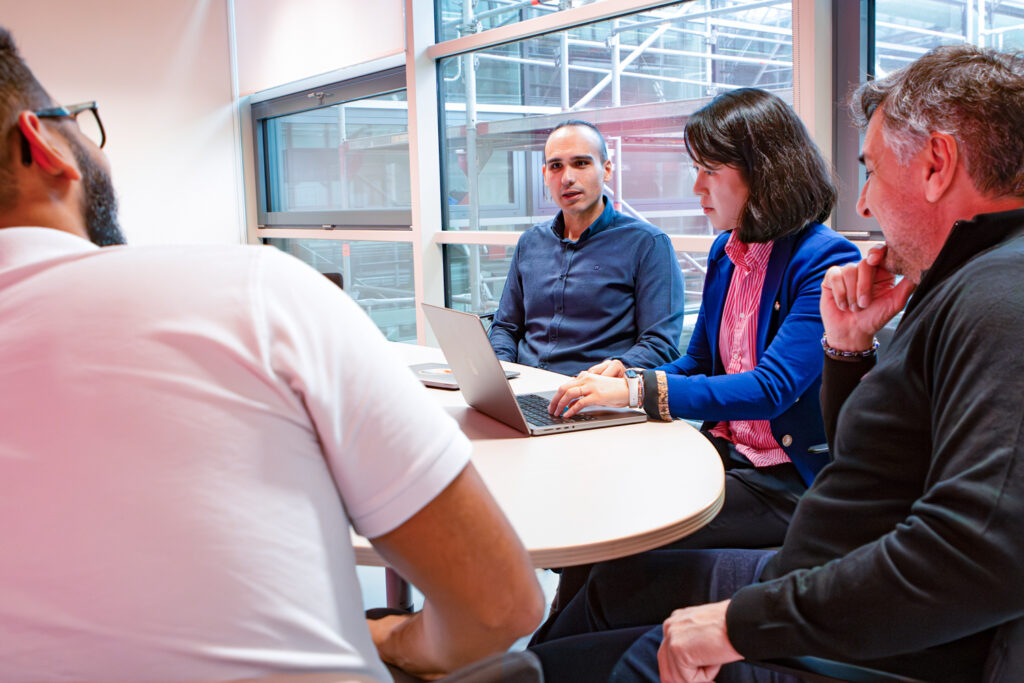 Four people discussing something at a table in front of a windowpane.